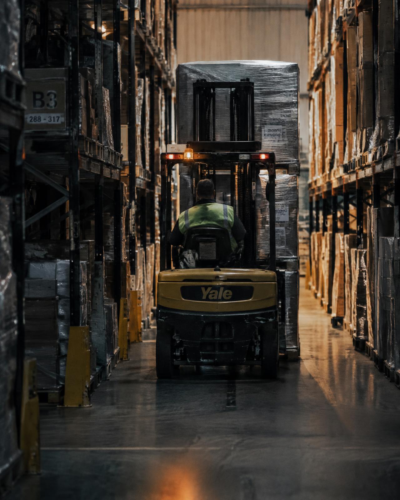 A forklift moving wrapped supplier stock through a racked warehouse aisle